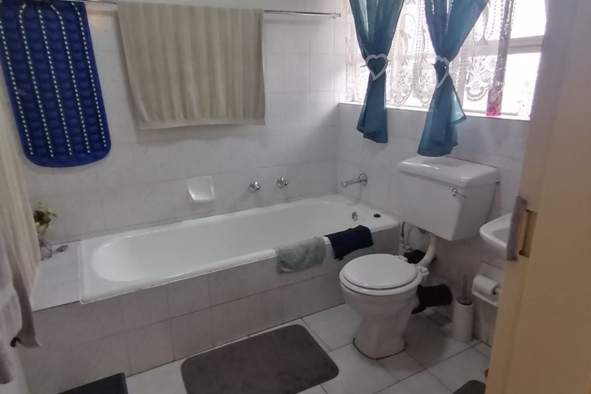 A functional bathroom featuring a built-in bathtub, toilet, and washbasin with tiled walls and flooring throughout.