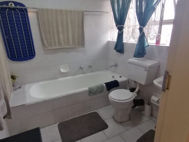 A functional bathroom featuring a built-in bathtub, toilet, and washbasin with tiled walls and flooring throughout.