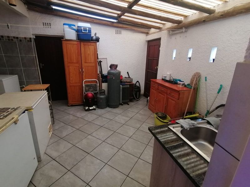 A functional laundry area featuring tiled flooring, a stainless steel sink, and a translucent roof with exposed timber rafters.