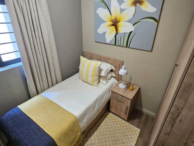 A compact, well-maintained bedroom featuring laminate flooring, a built-in wardrobe, and neutral wall tones.
