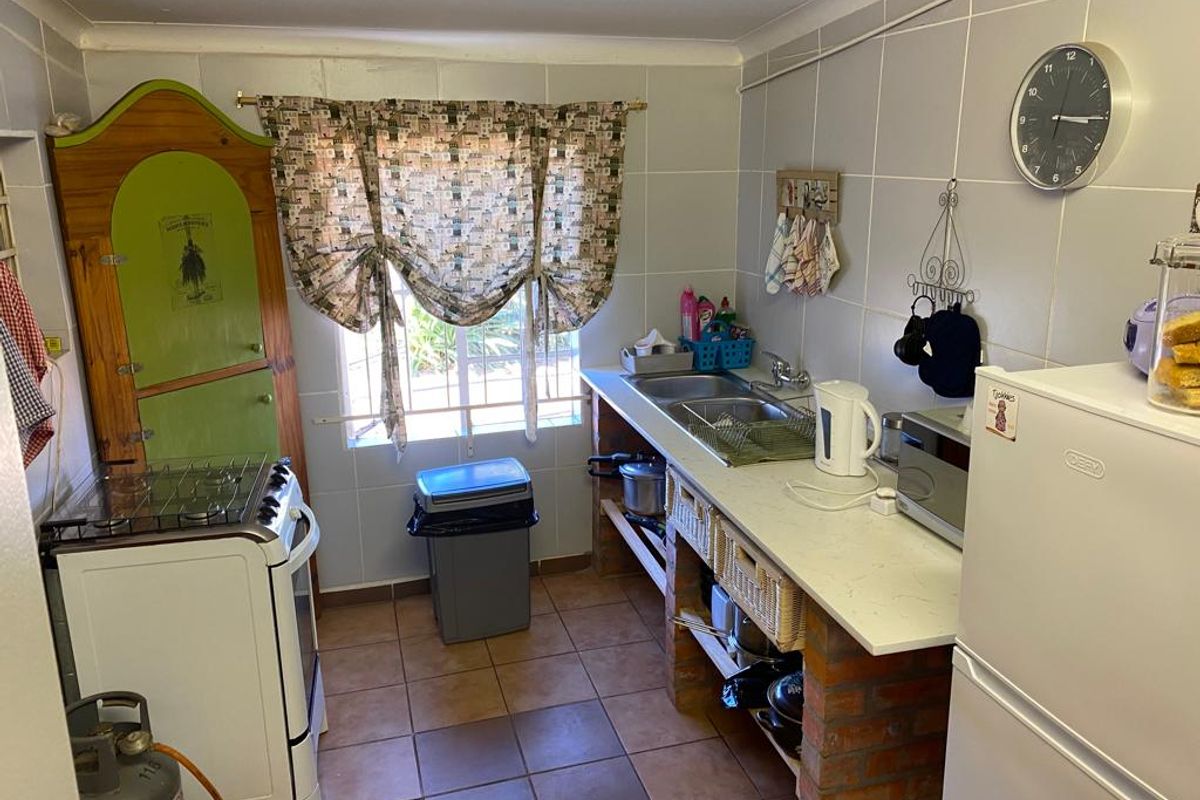 A compact kitchen featuring tiled walls, a gas stove, and a functional sink area with open brick-based shelving.