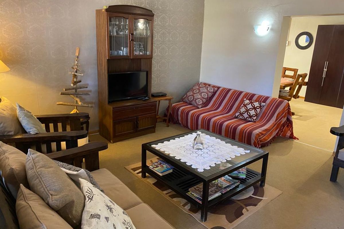 A comfortable living room featuring textured wallpaper, wall-to-wall carpeting, and a wall-mounted light fixture, with an open transition to the adjacent dining area.