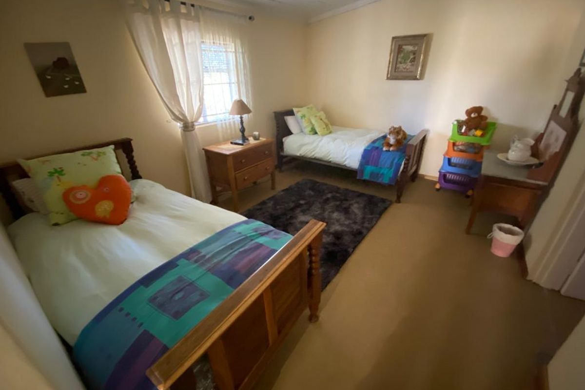A functional bedroom featuring neutral wall tones, carpeted flooring, and a window with natural light, suitable for a child's room or guest space.