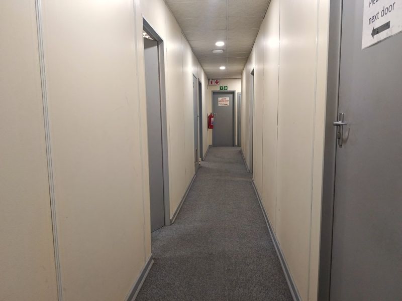 A functional commercial hallway featuring partition walls, recessed lighting, and carpeted flooring, providing access to multiple office or utility rooms.