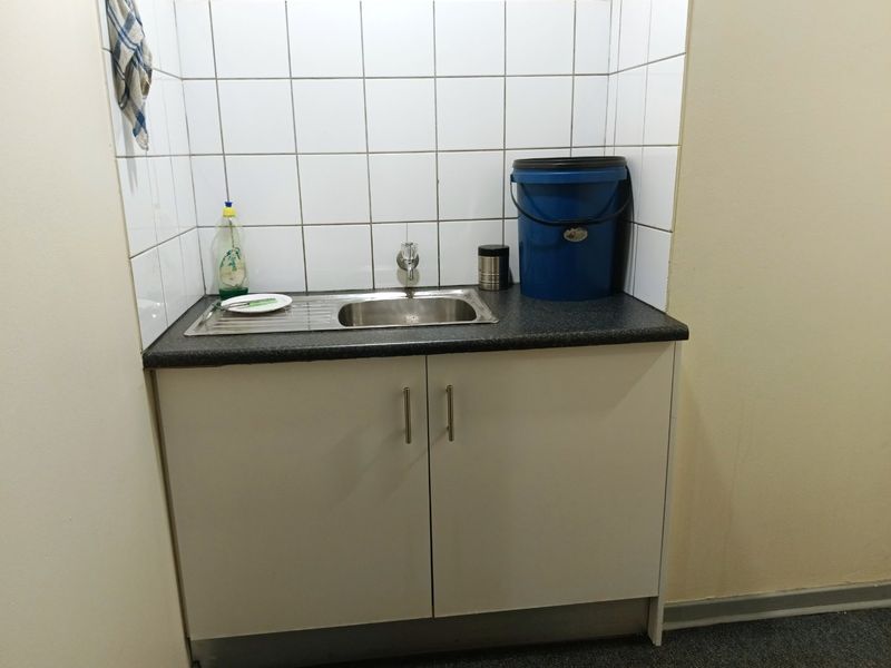 A functional scullery or utility area featuring a stainless steel sink, laminate countertop, and tiled splashback with built-in base cabinetry.