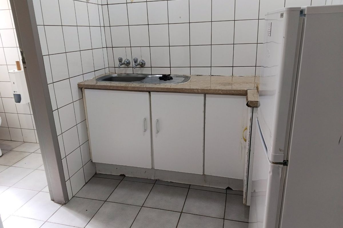 A compact kitchenette featuring a stainless steel sink, stone countertop, and tiled splashback, showing signs of wear and requiring cosmetic updates.