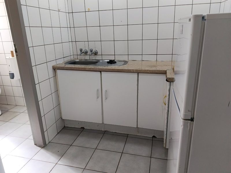 A compact kitchenette featuring a stainless steel sink, stone countertop, and tiled splashback, showing signs of wear and requiring cosmetic updates.