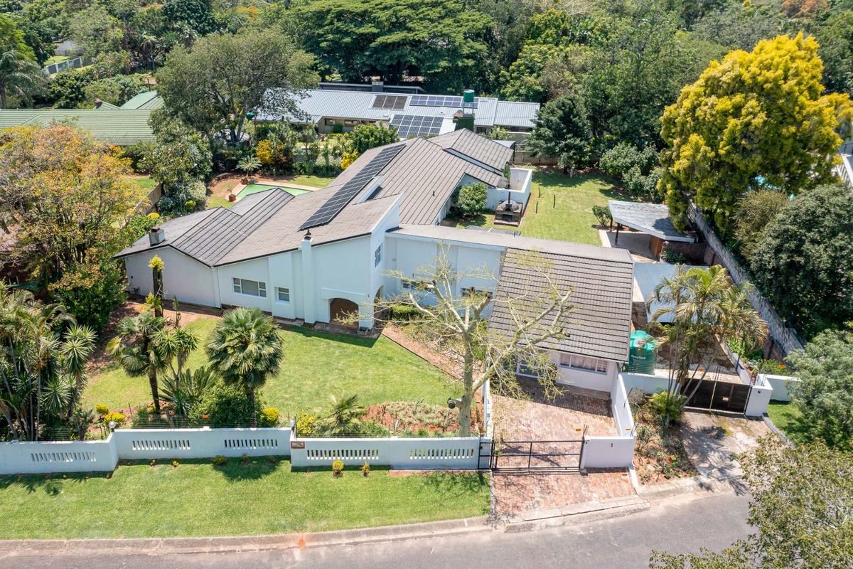 Aerial view of a residential property featuring a tiled roof with solar panels, a landscaped garden, brick driveway, and secure perimeter walling.