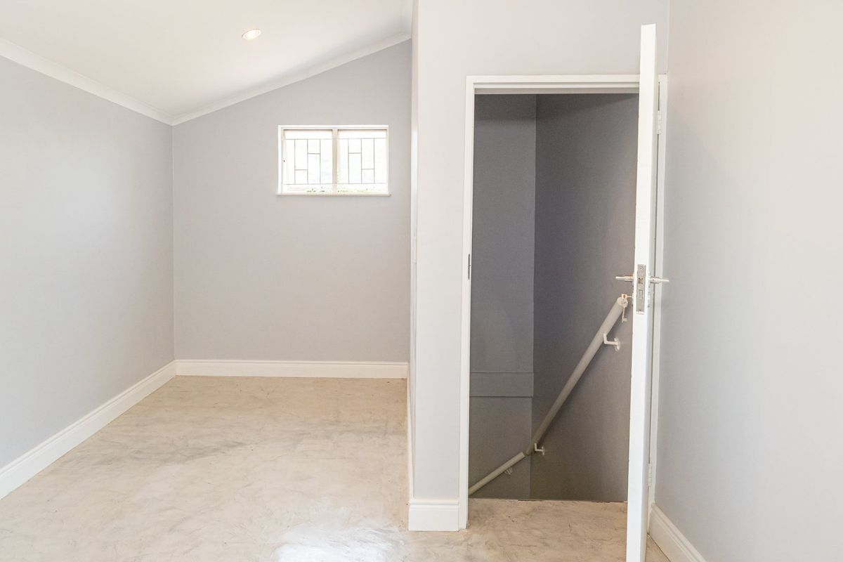 A clean, empty bedroom featuring neutral grey walls, recessed lighting, and a private staircase leading to a lower level.