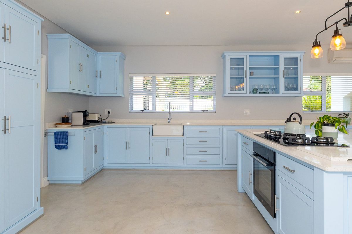 Modern kitchen featuring light blue cabinetry, quartz countertops, an apron-front sink, integrated gas cooktop, built-in oven, and polished concrete flooring.