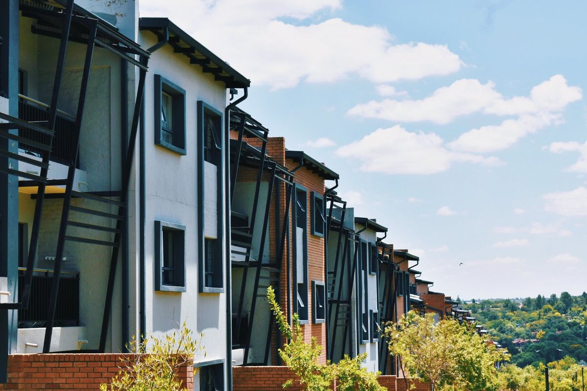A view of the rear elevation of a modern apartment complex featuring brick and rendered facades with integrated balconies and metal detailing.