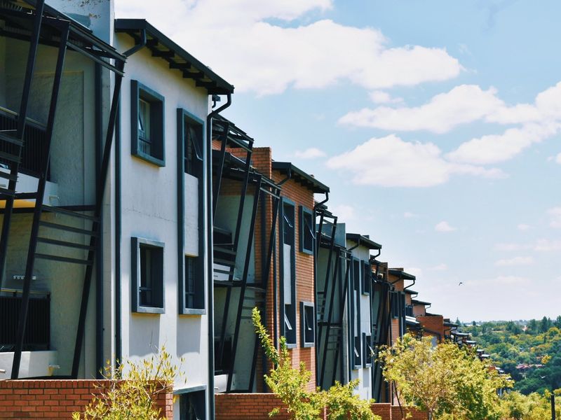 A view of the rear elevation of a modern apartment complex featuring brick and rendered facades with integrated balconies and metal detailing.