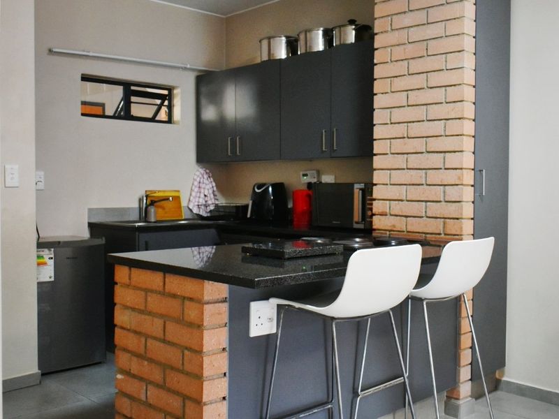Compact kitchen featuring dark cabinetry, granite countertops, and a unique brick-accented breakfast bar with tiled flooring.