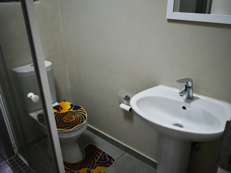 A functional bathroom featuring a pedestal basin, toilet, and a glass-enclosed shower with neutral wall finishes and tiled flooring.