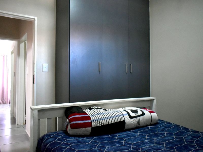 A bedroom featuring a dark-toned built-in wardrobe and tiled flooring, with a view into the adjacent hallway.
