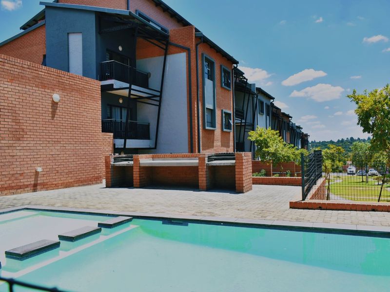Communal pool area featuring a paved patio, built-in brick braai facility, and secure perimeter fencing within the apartment complex.