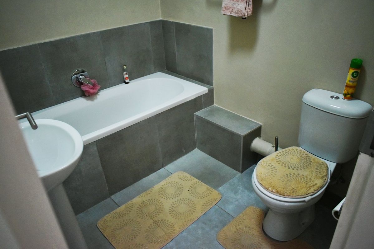 A functional bathroom featuring a bathtub with grey tiling, a pedestal basin, and a standard toilet.