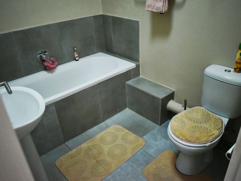 A functional bathroom featuring a bathtub with grey tiling, a pedestal basin, and a standard toilet.