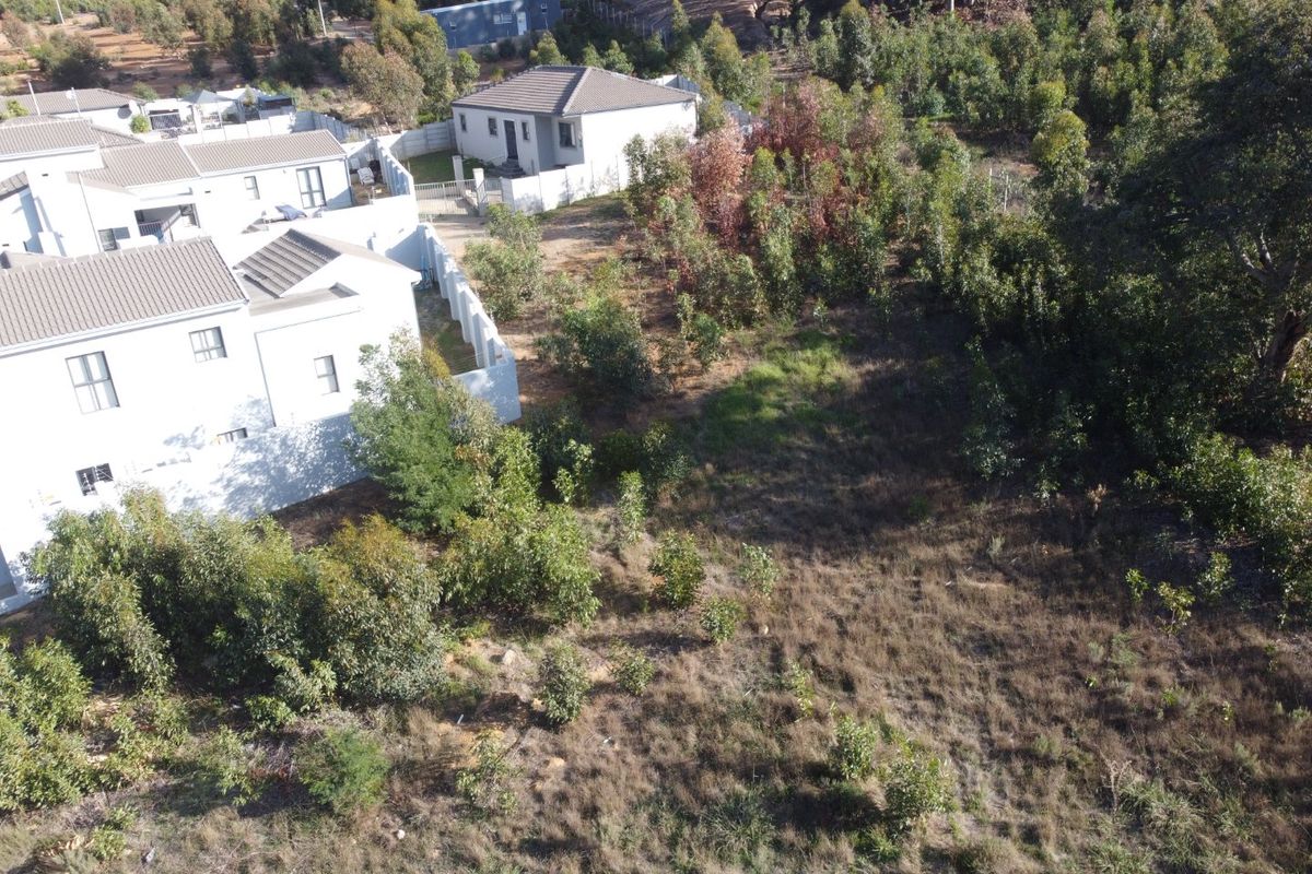 Aerial view of a vacant residential plot situated adjacent to existing housing developments, featuring natural vegetation and perimeter boundary walls.