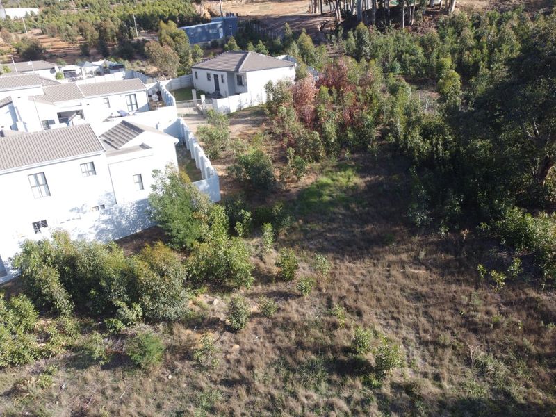 Aerial view of a vacant residential plot situated adjacent to existing housing developments, featuring natural vegetation and perimeter boundary walls.