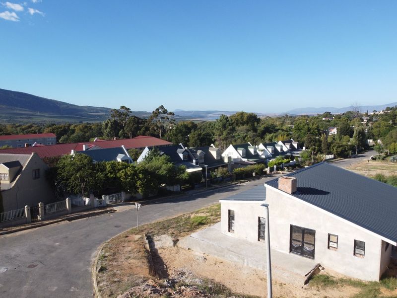 Aerial view of a residential street featuring a property under construction with an unfinished exterior and metal roofing in a scenic neighborhood setting.