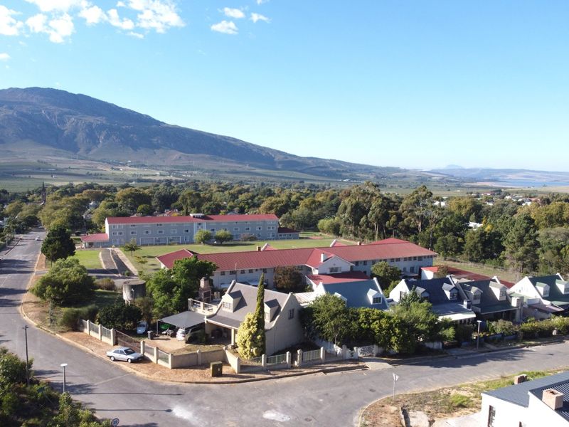 An aerial view of a residential neighborhood featuring multiple buildings with pitched roofs, surrounded by mature trees and local road infrastructure.