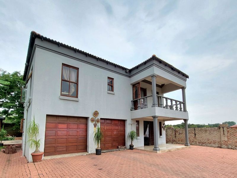 Two-story residential property featuring a double garage, upper-level balcony with balustrades, and a spacious brick-paved driveway.