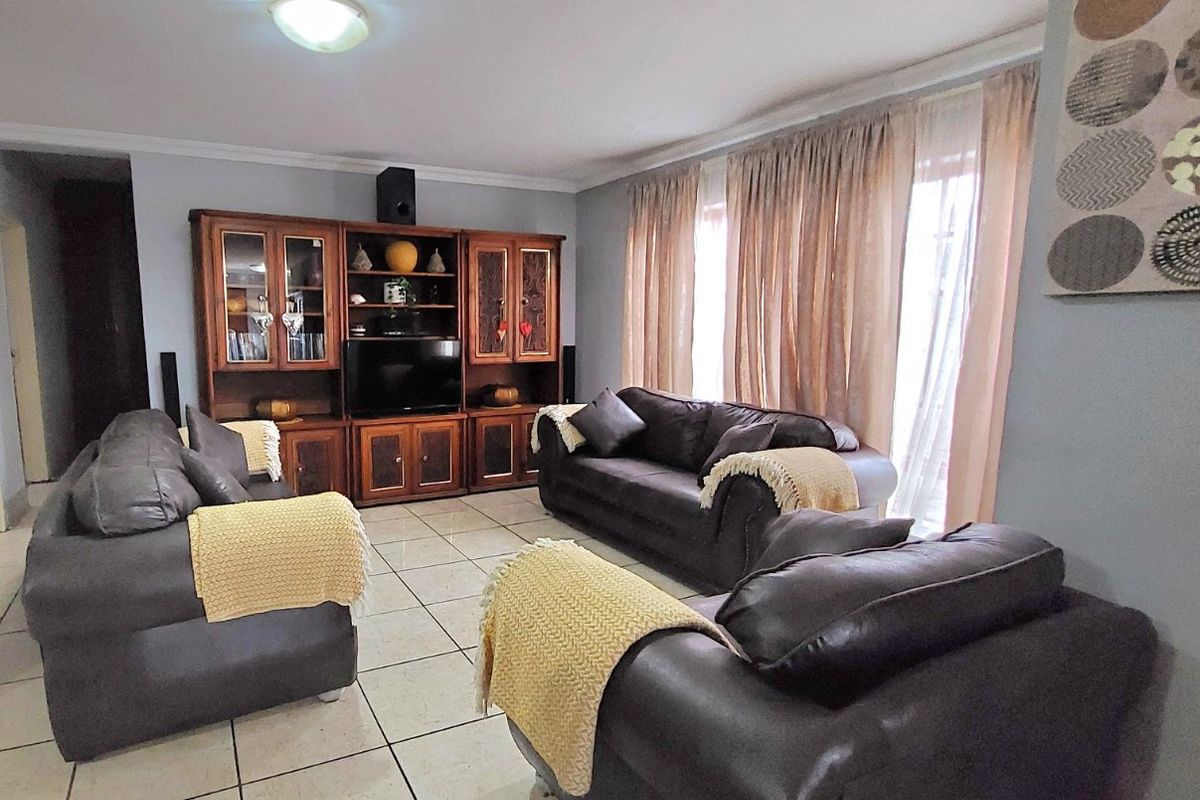 A spacious living room featuring ceramic floor tiles, neutral wall finishes, and large windows with curtains, providing a comfortable and functional living space.