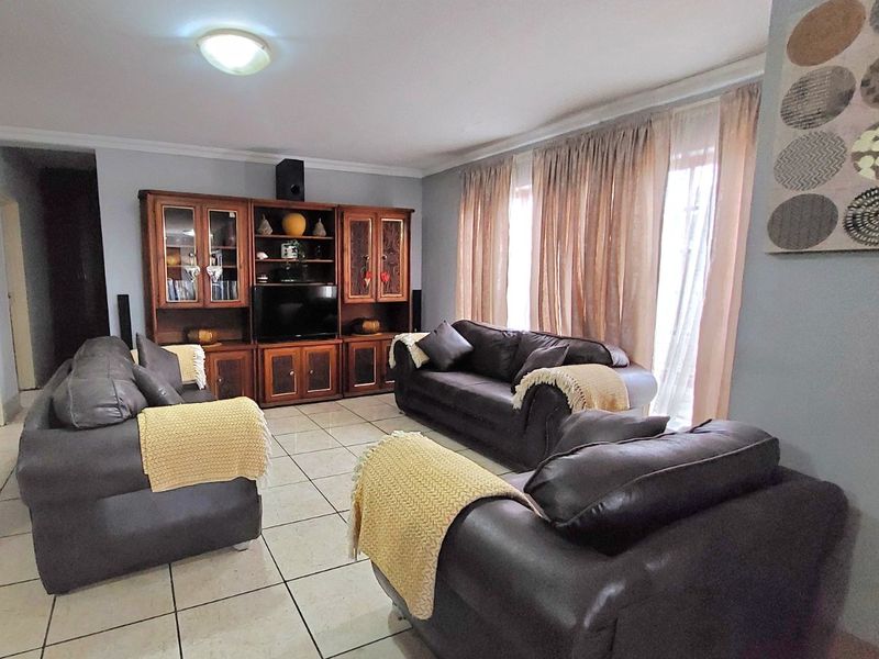 A spacious living room featuring ceramic floor tiles, neutral wall finishes, and large windows with curtains, providing a comfortable and functional living space.