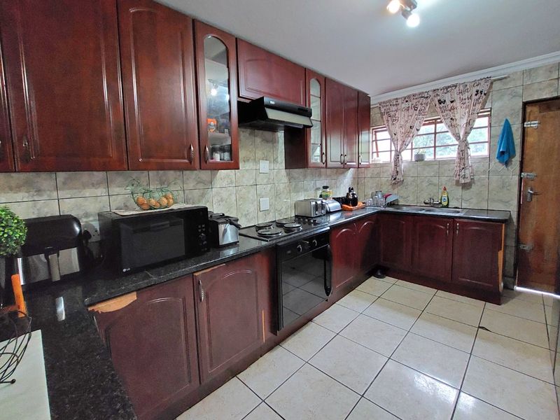 A functional kitchen featuring dark wood cabinetry, granite countertops, built-in oven and hob, and tiled flooring, offering a classic layout with potential for modernization.
