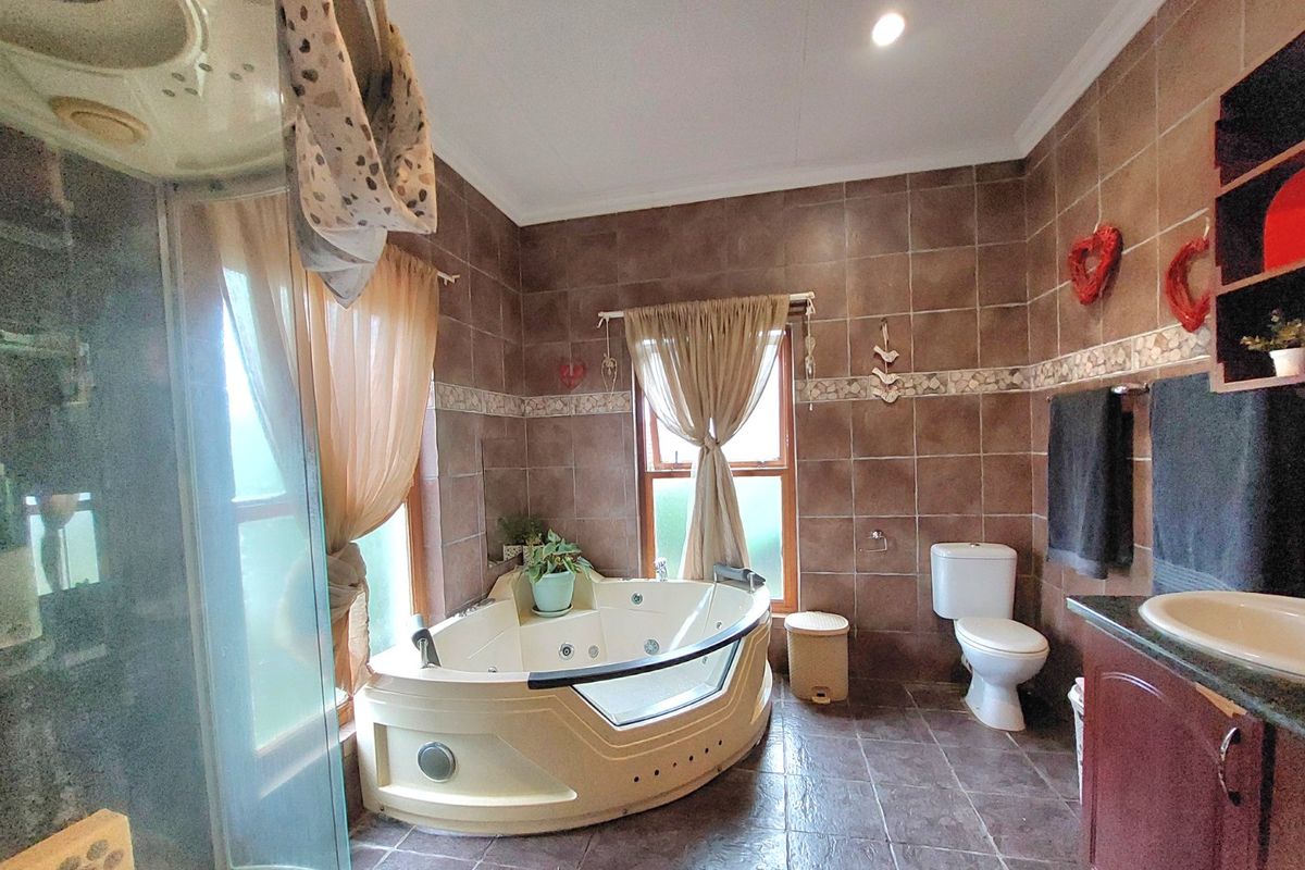 A spacious bathroom featuring a corner spa bath, separate shower enclosure, vanity unit, and full-height brown ceramic wall tiling.