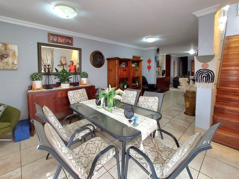 A dining area featuring tiled flooring and a wooden staircase, leading into an open-plan living space with neutral wall finishes.