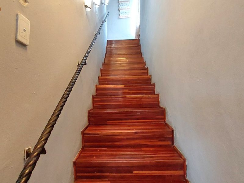 A narrow hallway featuring a wooden staircase with a decorative metal handrail and wall-mounted lighting.