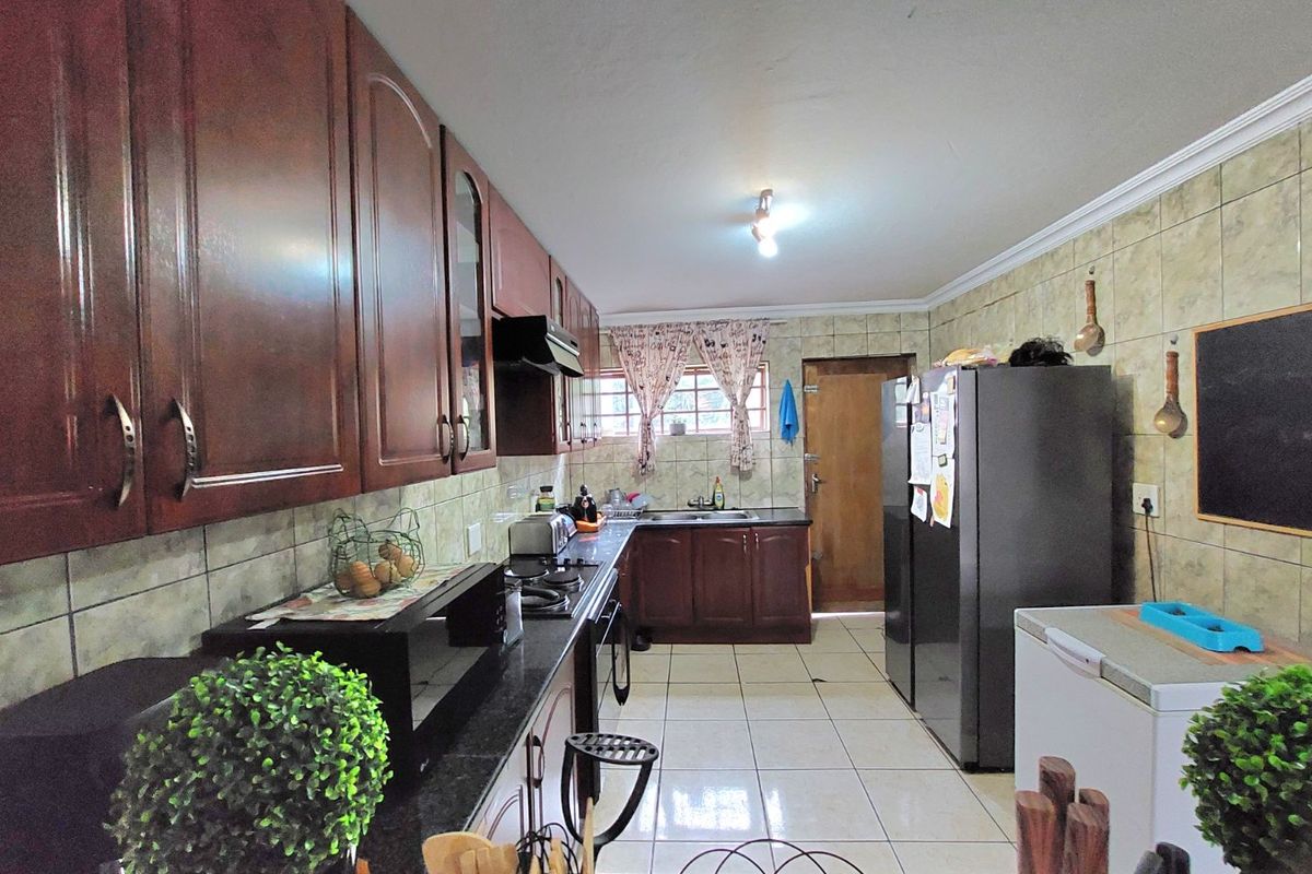A functional kitchen featuring dark wood cabinetry, granite countertops, tiled backsplash, and tiled flooring, providing ample storage and workspace.