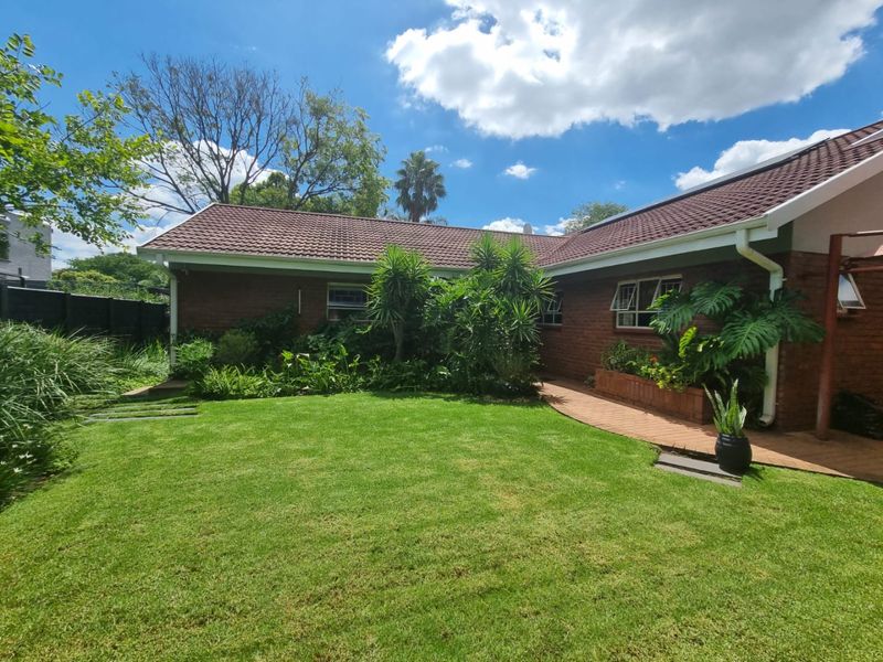 A well-maintained rear garden featuring a lush lawn, brick-paved patio area, and established landscaping against a classic brick house exterior.