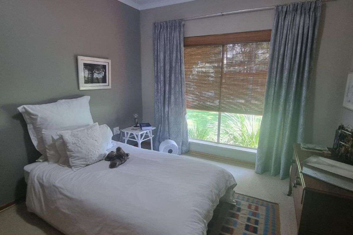 A cozy bedroom featuring neutral wall tones, carpeted flooring, and large windows with integrated blinds and curtain rails for natural light control.