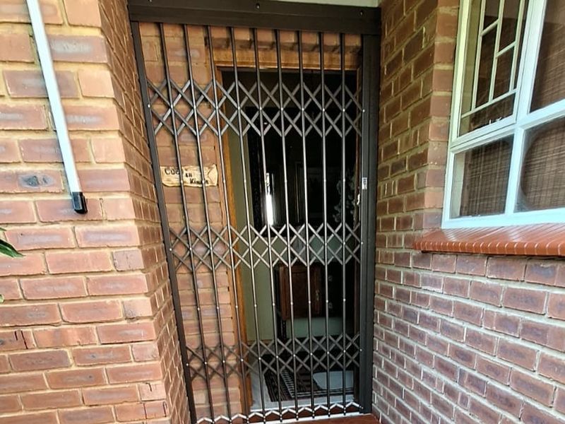 A secure residential entrance featuring a retractable metal security gate, brick exterior walls, and a covered tiled threshold with overhead lighting.