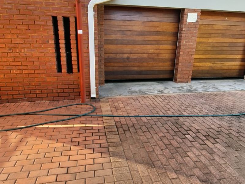 A double garage with wooden doors and a paved driveway area featuring a shade sail structure.