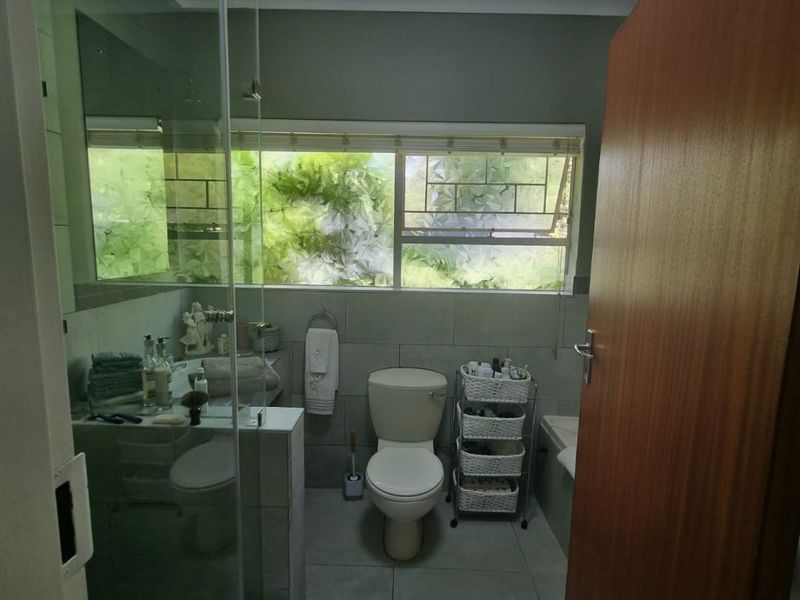 A functional bathroom featuring a glass-enclosed shower, bathtub, toilet, and neutral wall and floor tiling with a window for natural light.