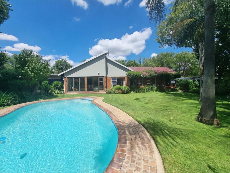 Rear view of the property featuring a well-maintained swimming pool, brick coping, expansive lawn, and a modernised rear facade with large sliding glass doors.