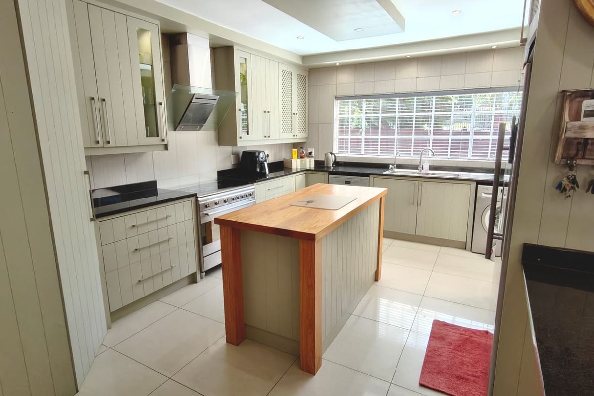 A well-appointed kitchen featuring sage green cabinetry, a central wooden island, granite countertops, and modern stainless steel appliances.