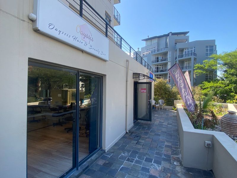 Commercial storefront entrance featuring a stone-paved patio, sliding glass doors, and prominent business signage, suitable for a hair and beauty salon.