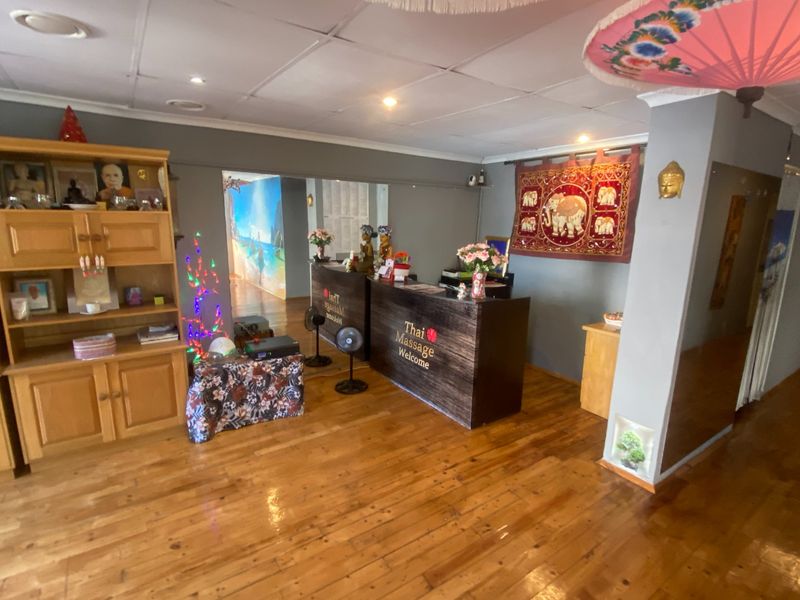 Commercial reception area featuring timber flooring, a built-in reception desk, and recessed ceiling lighting, suitable for a professional wellness or massage business.