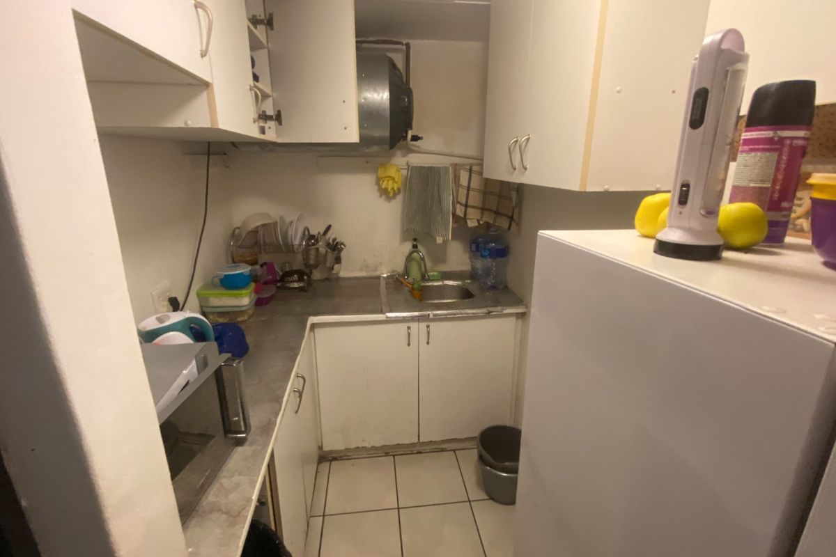 A compact kitchen area featuring built-in cabinetry, a stainless steel sink, and tiled flooring, currently showing signs of wear and dated finishes.
