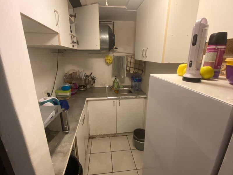 A compact kitchen area featuring built-in cabinetry, a stainless steel sink, and tiled flooring, currently showing signs of wear and dated finishes.