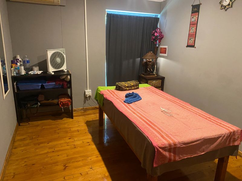 A functional commercial room featuring polished hardwood flooring and a wall-mounted air conditioning unit, currently utilized as a treatment space.