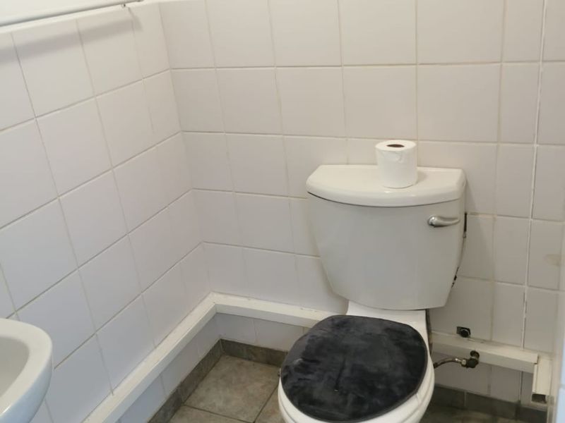 A functional commercial bathroom featuring a standard toilet, white wall tiling, and tiled flooring.