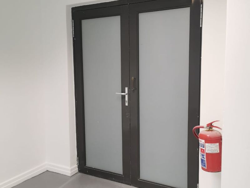 A clean utility or hallway area featuring double glass doors, emergency exit signage, and a wall-mounted fire extinguisher.