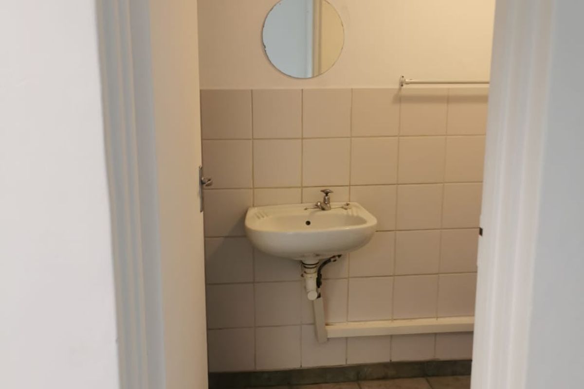 A small, functional bathroom featuring a wall-mounted basin, tiled walls, and tiled flooring, currently presented in a basic, vacant condition.