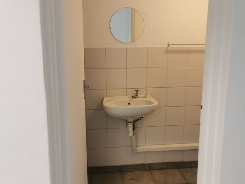 A small, functional bathroom featuring a wall-mounted basin, tiled walls, and tiled flooring, currently presented in a basic, vacant condition.